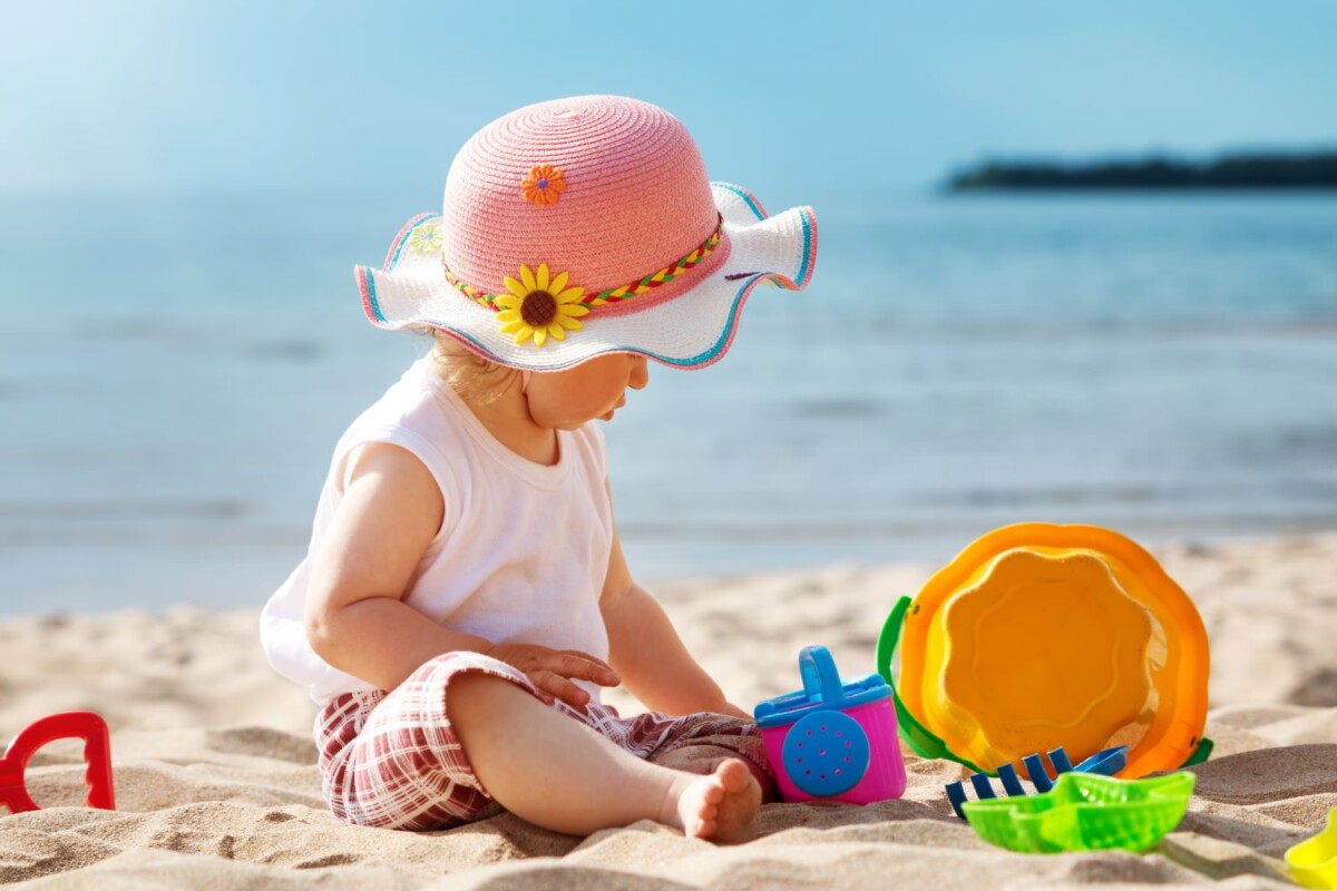 A baby in a hat plays on a beach
